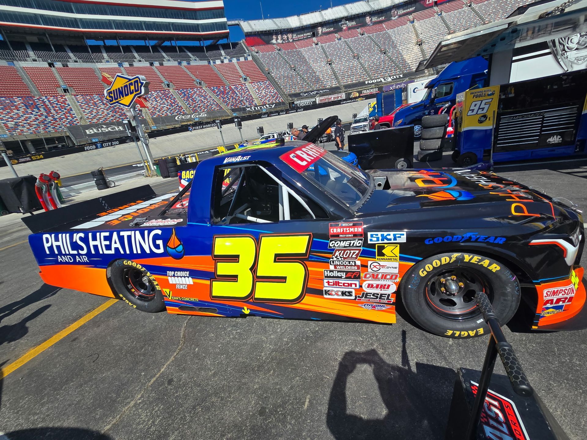 Blue-and-orange #35 race truck in a stadium pit lane, with PHYS HEATING on the side