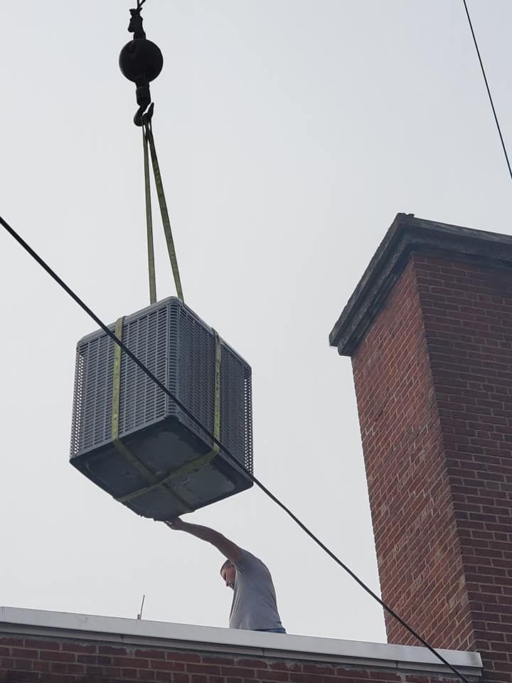 Crane lifting a large metal crate above a brick building as a worker reaches up from below