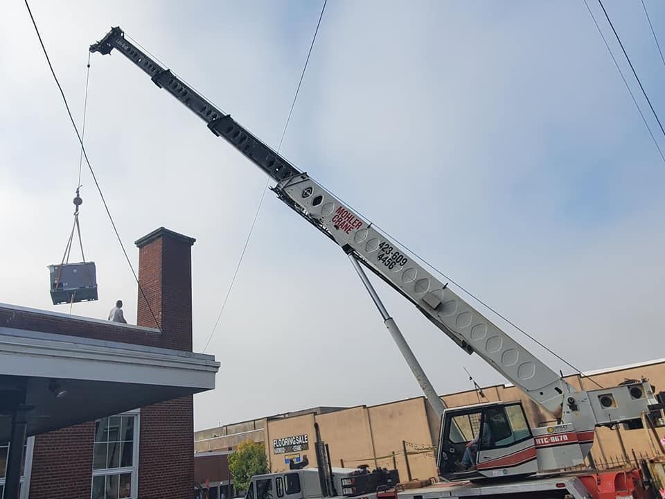 Crane lifting a hanging load near a building roof and chimney at a construction site