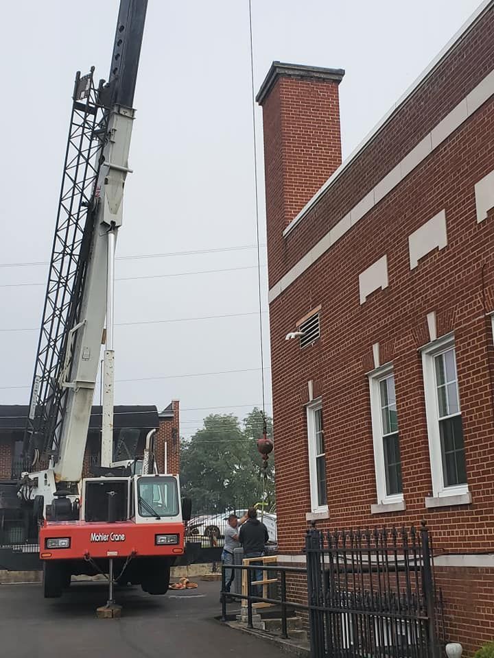 Crane beside a red brick building on a wet street, with workers nearby.