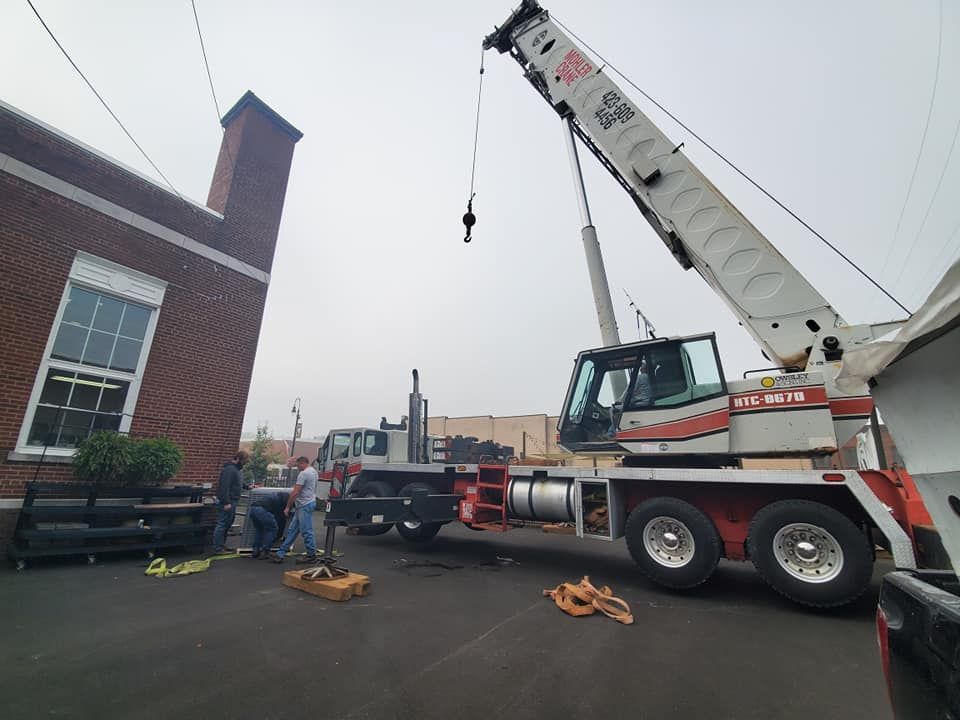 Crane lifting material beside a brick building on a construction site, with workers and trucks nearby