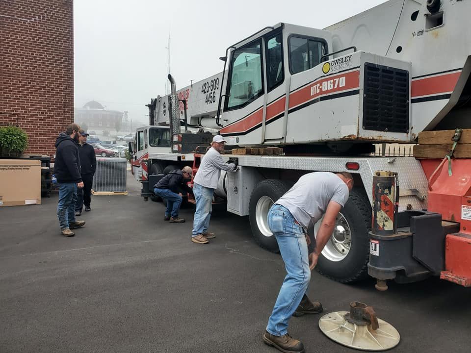 Workers servicing a white utility truck in a parking lot, one using a floor buffer near the rear wheel.