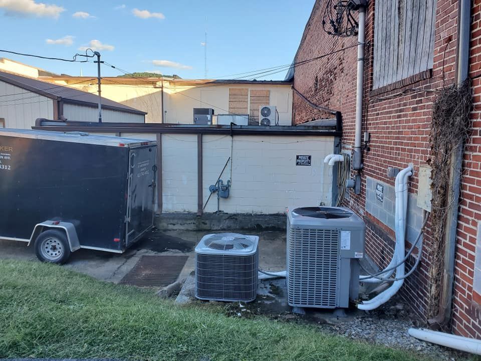 Backyard with parked black trailer, two air-conditioning units, and brick buildings at dusk