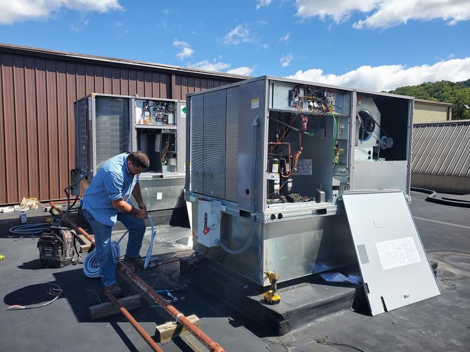 Technician works on an outdoor HVAC unit with its panel open beside a building