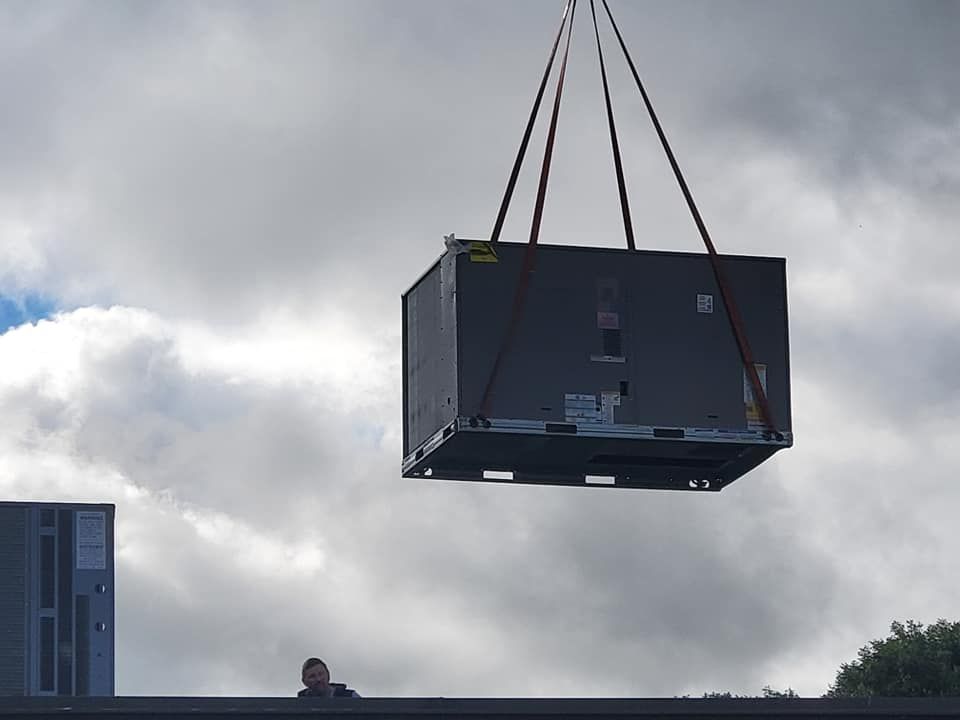 Large dark crate being lifted by crane against a cloudy sky