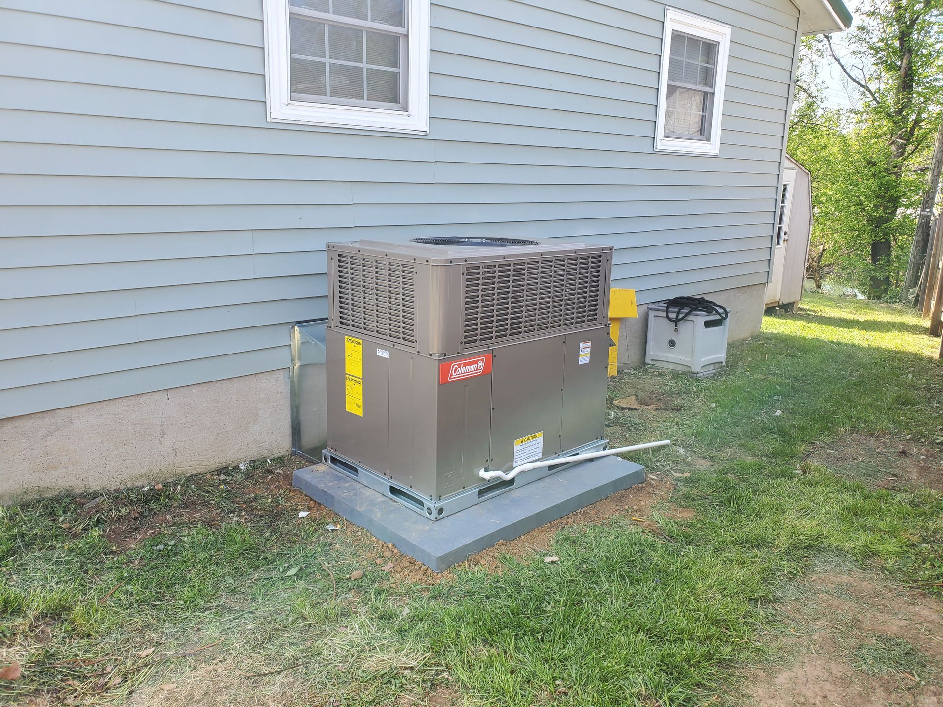 Outdoor HVAC unit beside a blue house with a grassy yard and trees in the background