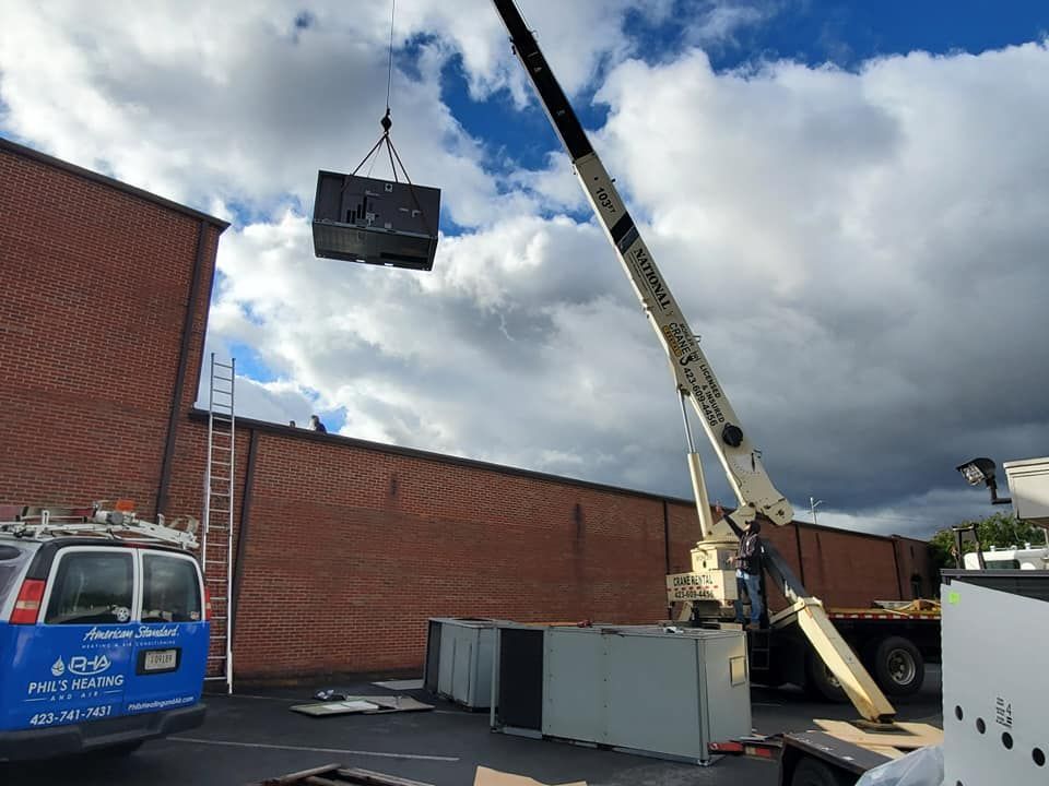 Crane lifting a large unit over a brick wall beside a blue van at a construction site