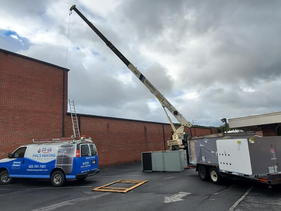 Utility truck and crane lifting equipment beside a brick building under a cloudy sky