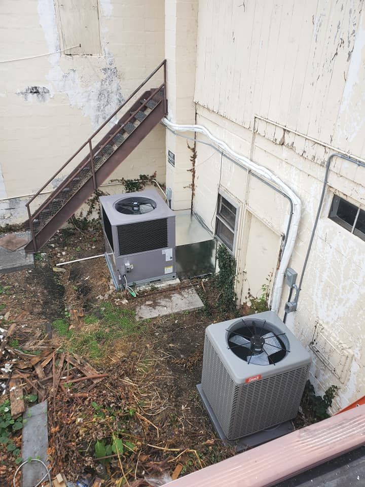 Two gray outdoor HVAC units beside a beige building wall and a metal staircase.