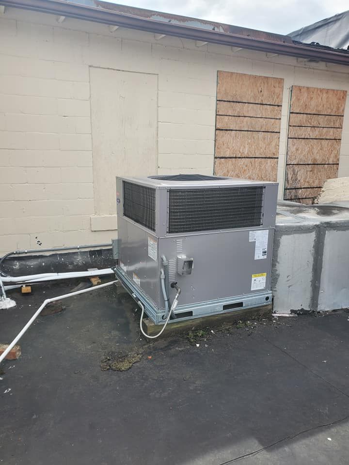 Large rooftop HVAC unit beside a beige wall with boarded-up windows and electrical conduit.
