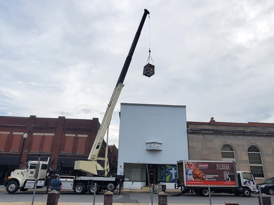 Contact Us Crane hoisting a load above a white storefront on a city street with trucks parked below