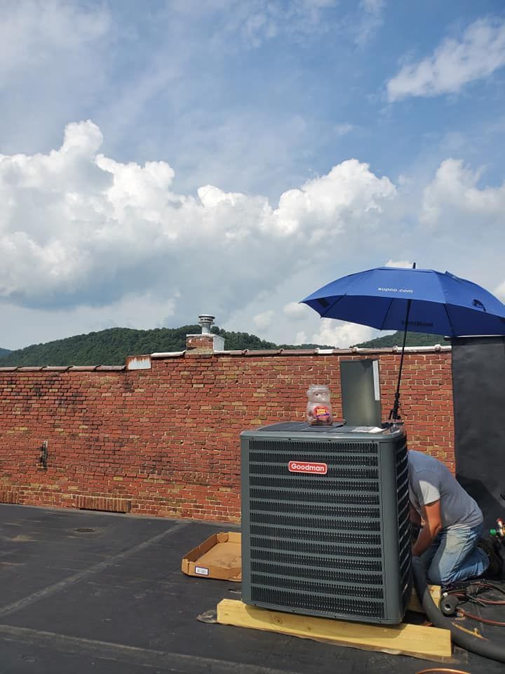 Rooftop HVAC unit under a blue umbrella beside a brick parapet, with a partly cloudy sky above.