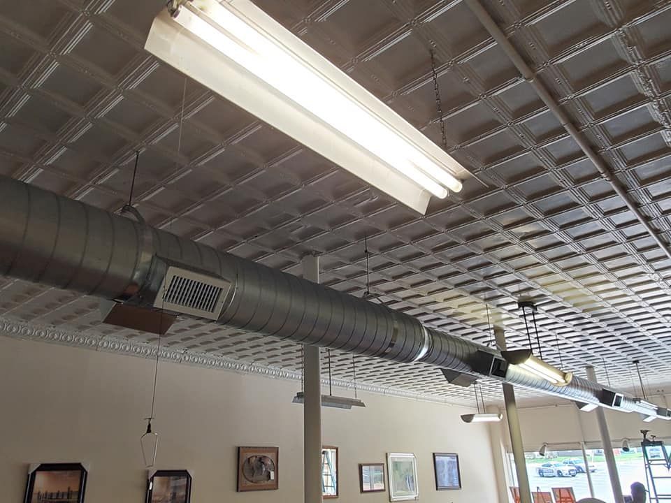 Ceiling in a bright cafe with fluorescent lights, exposed ductwork, and framed wall art