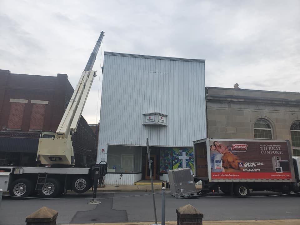 Crane truck beside a white building, with a red advertising truck parked nearby.