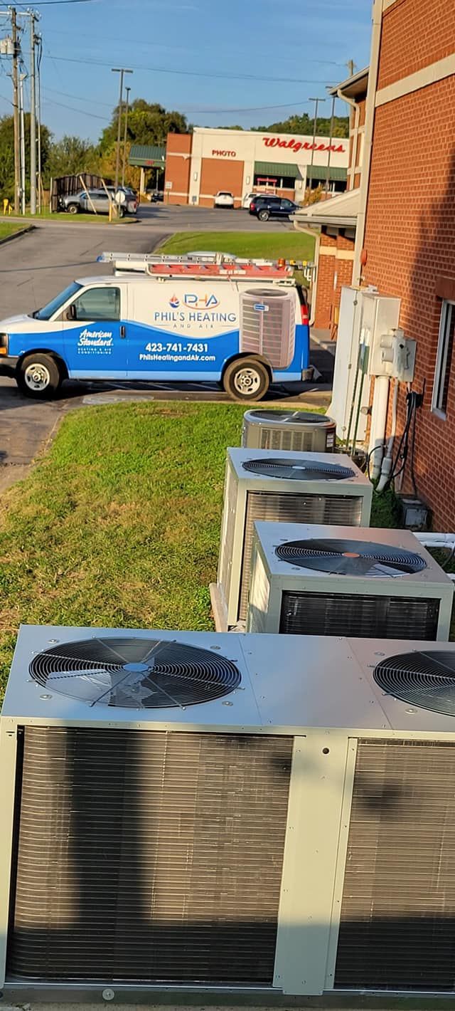 Several HVAC units beside a brick building, with a blue service van parked on a street in the background