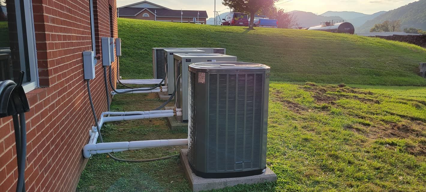 Row of outdoor HVAC units beside a brick building beside a grassy field at sunset