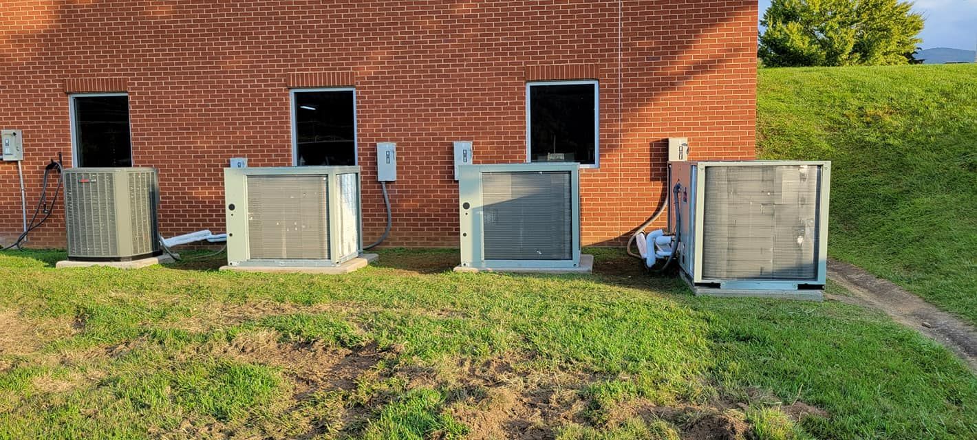 Four outdoor HVAC units beside a brick building with grass and a hedge