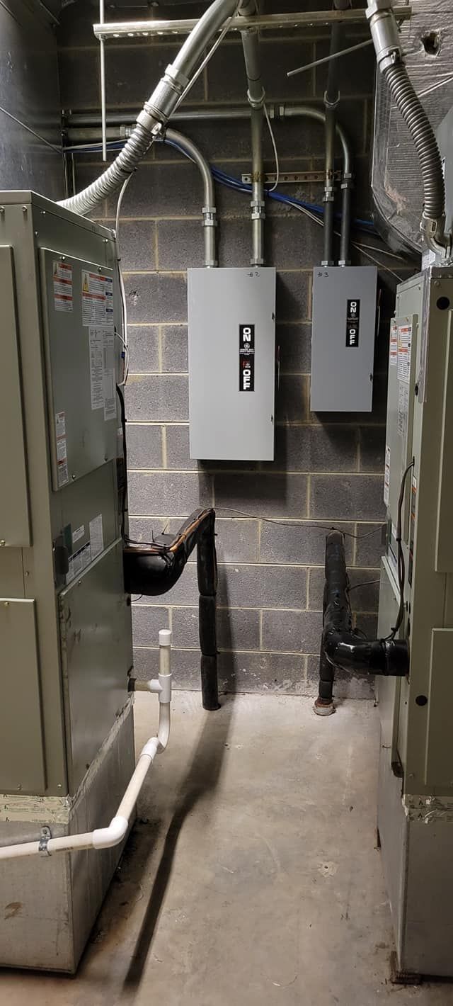 Basement utility room with electrical panels, exposed pipes, and cinderblock walls.