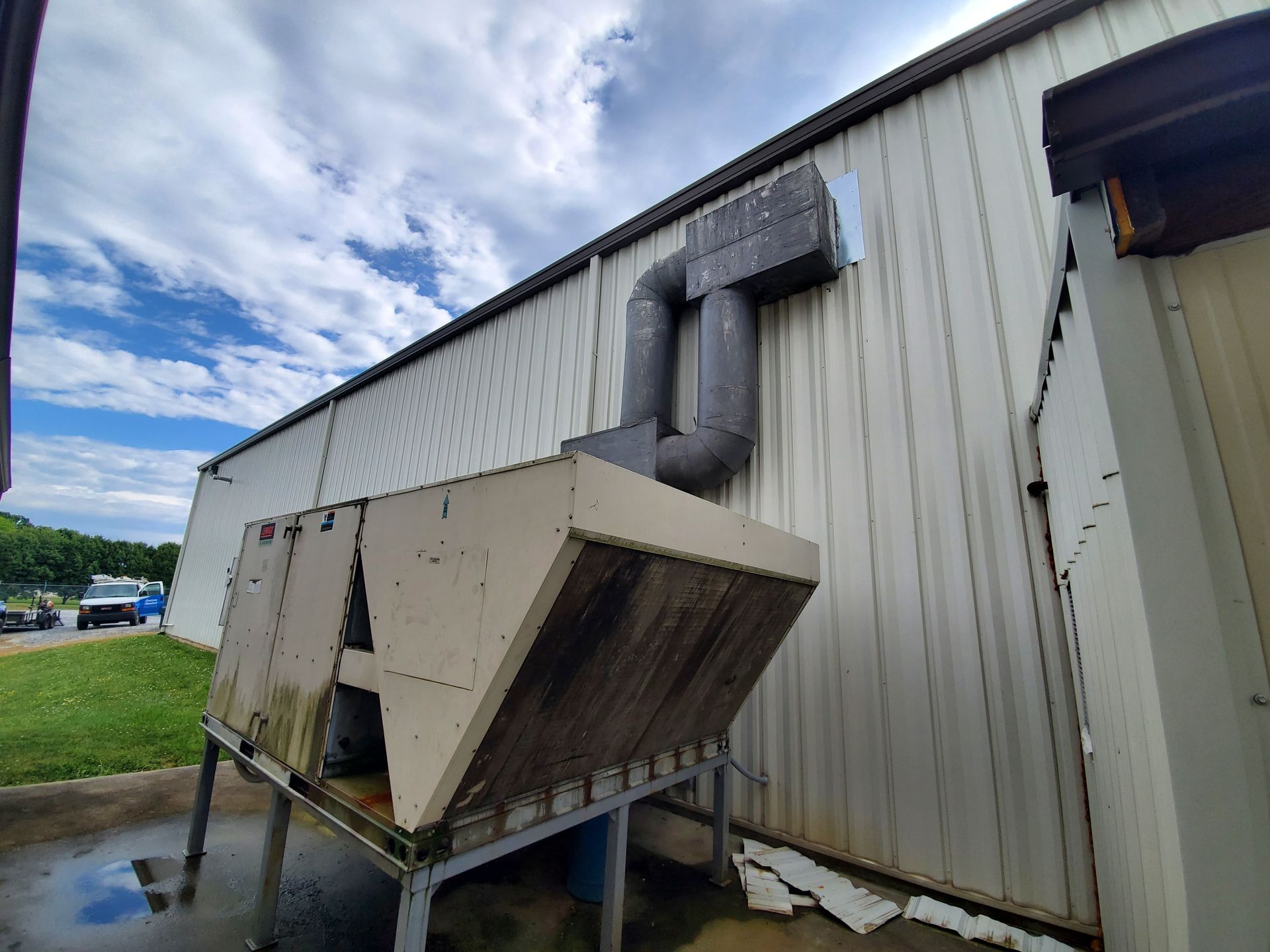 Outdoor industrial HVAC unit with large metal ductwork beside a beige building, above a wet concrete pad