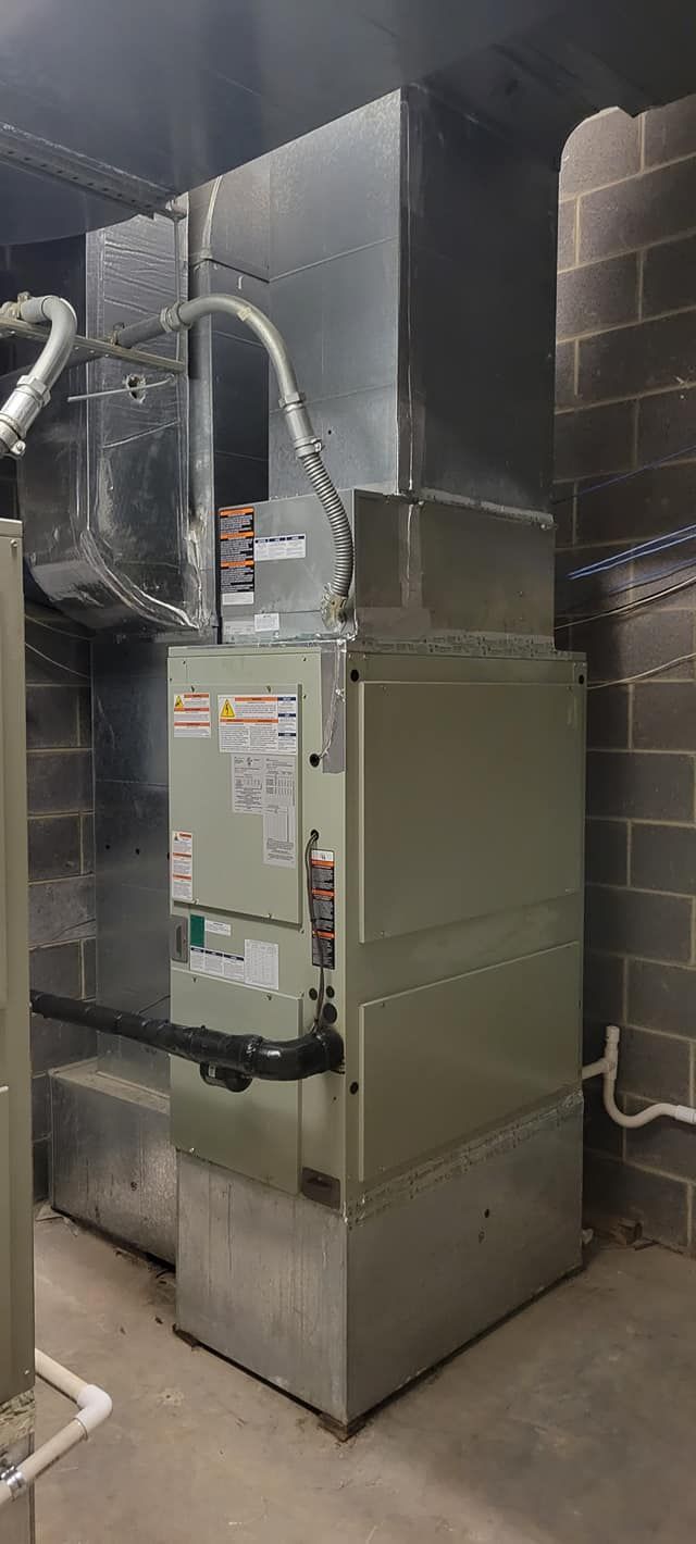 Commercial HVAC furnace in a utility room with metal ductwork and gray insulation panels.