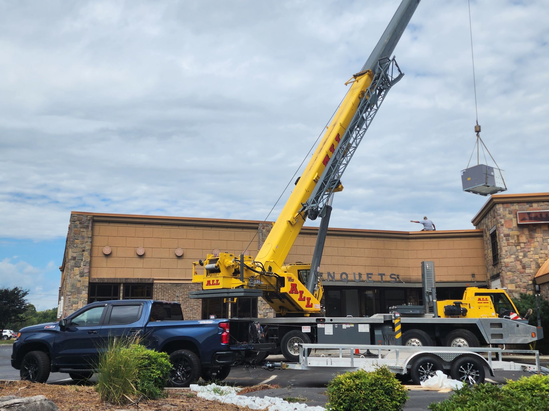 Tow truck lifting a car in front of a brick building, with a crane and blue pickup nearby