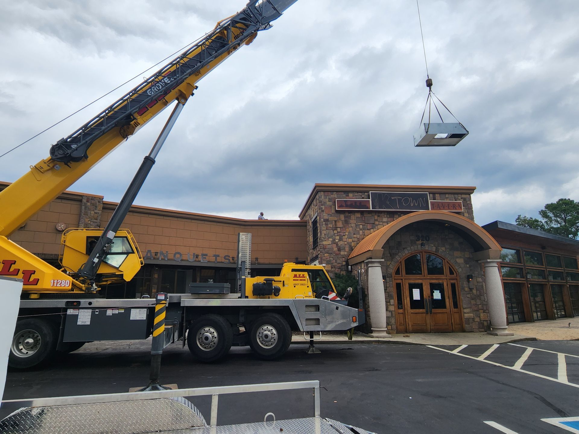 Crane lifting a large object over a brick building entrance on a cloudy day