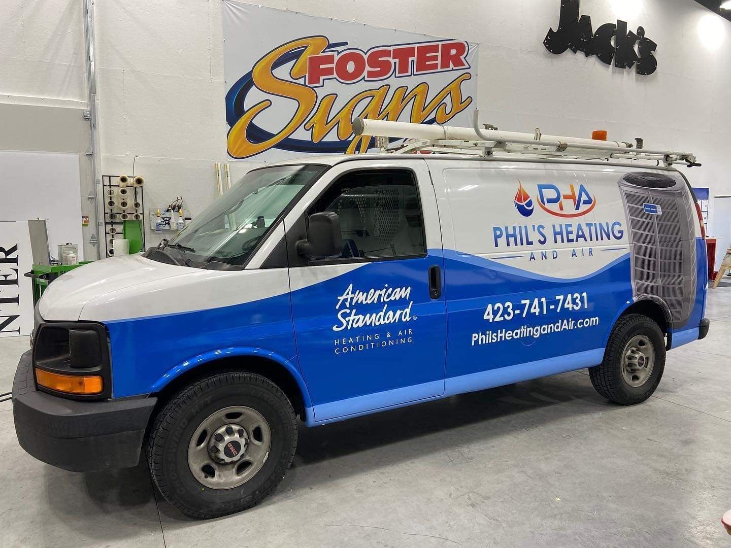 Blue-and-white Phillips Heating service van parked indoors with company logos and phone number on the side