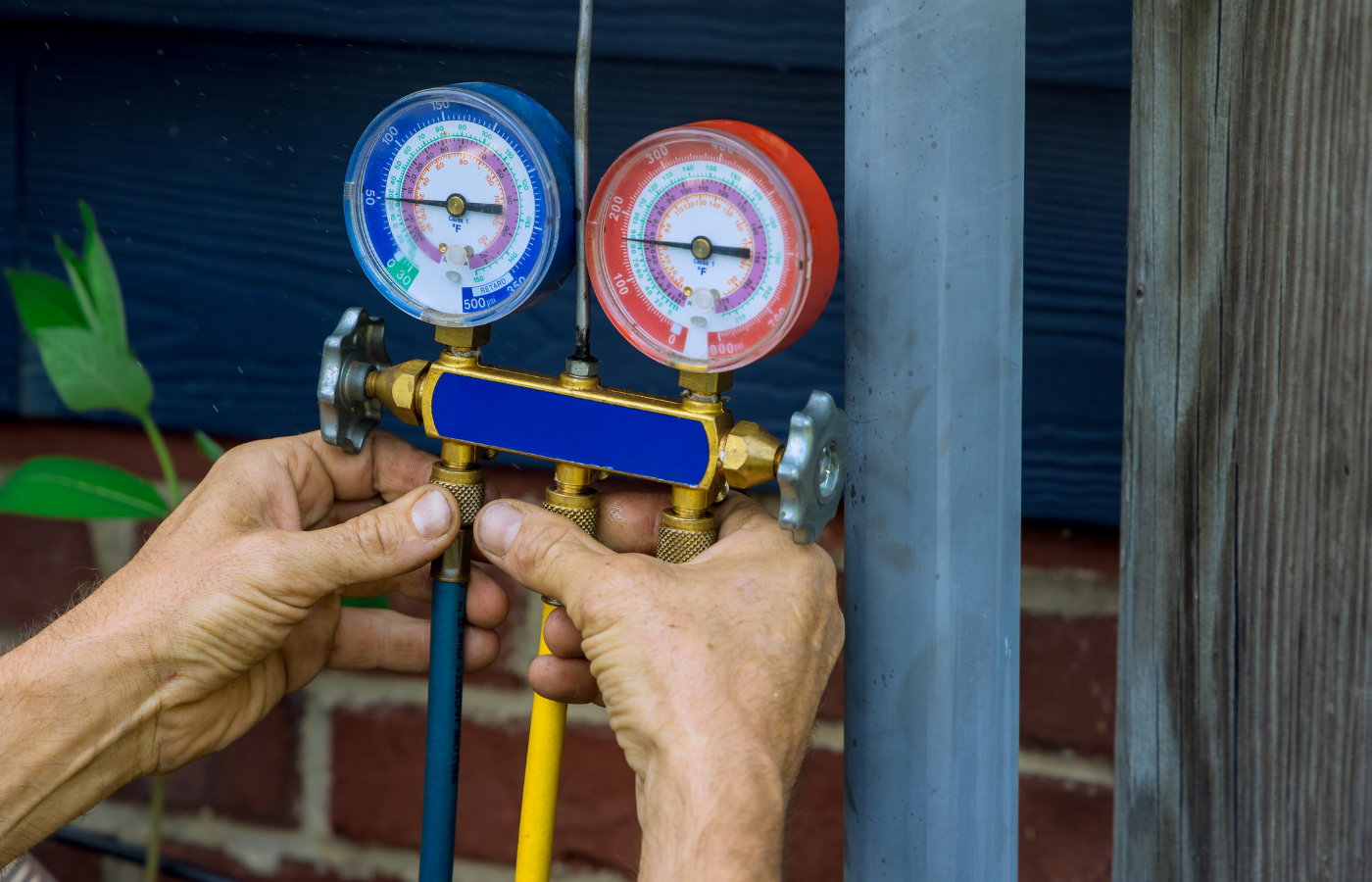 Hands attaching gauges to a blue manifold on outdoor HVAC service lines