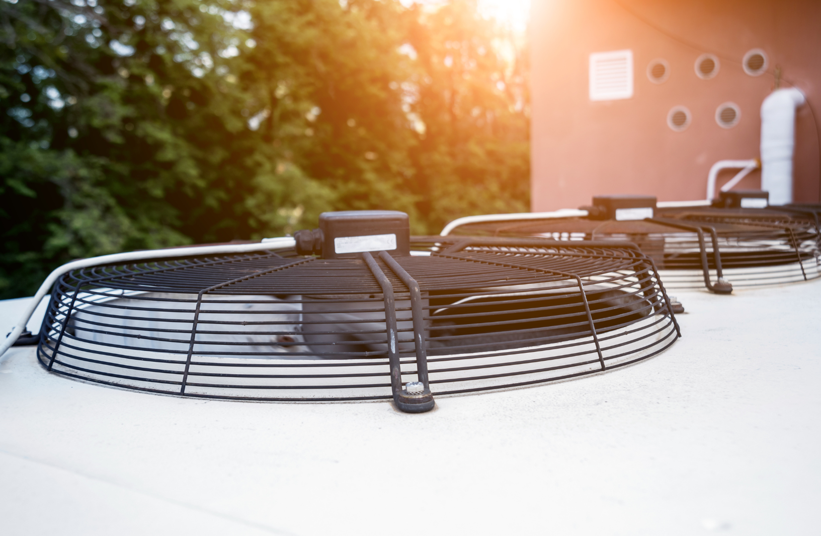 Our Services Air conditioner unit on a rooftop at sunset, with a protective metal fan guard in front.