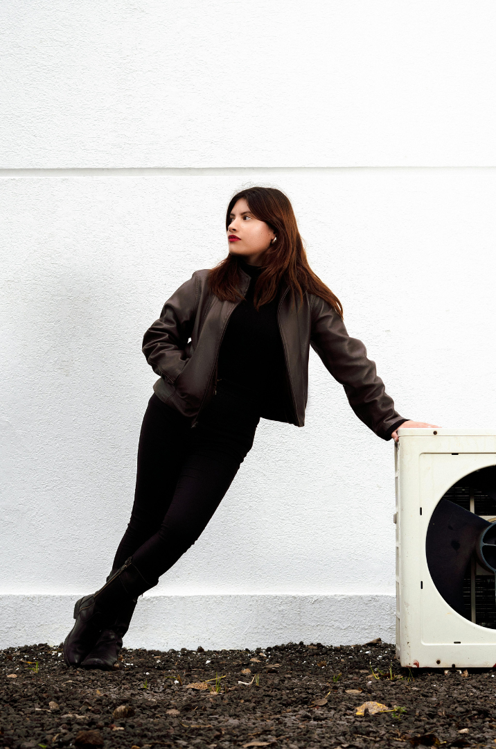 Contact Us! Woman leaning against a white wall beside an outdoor air-conditioning unit.