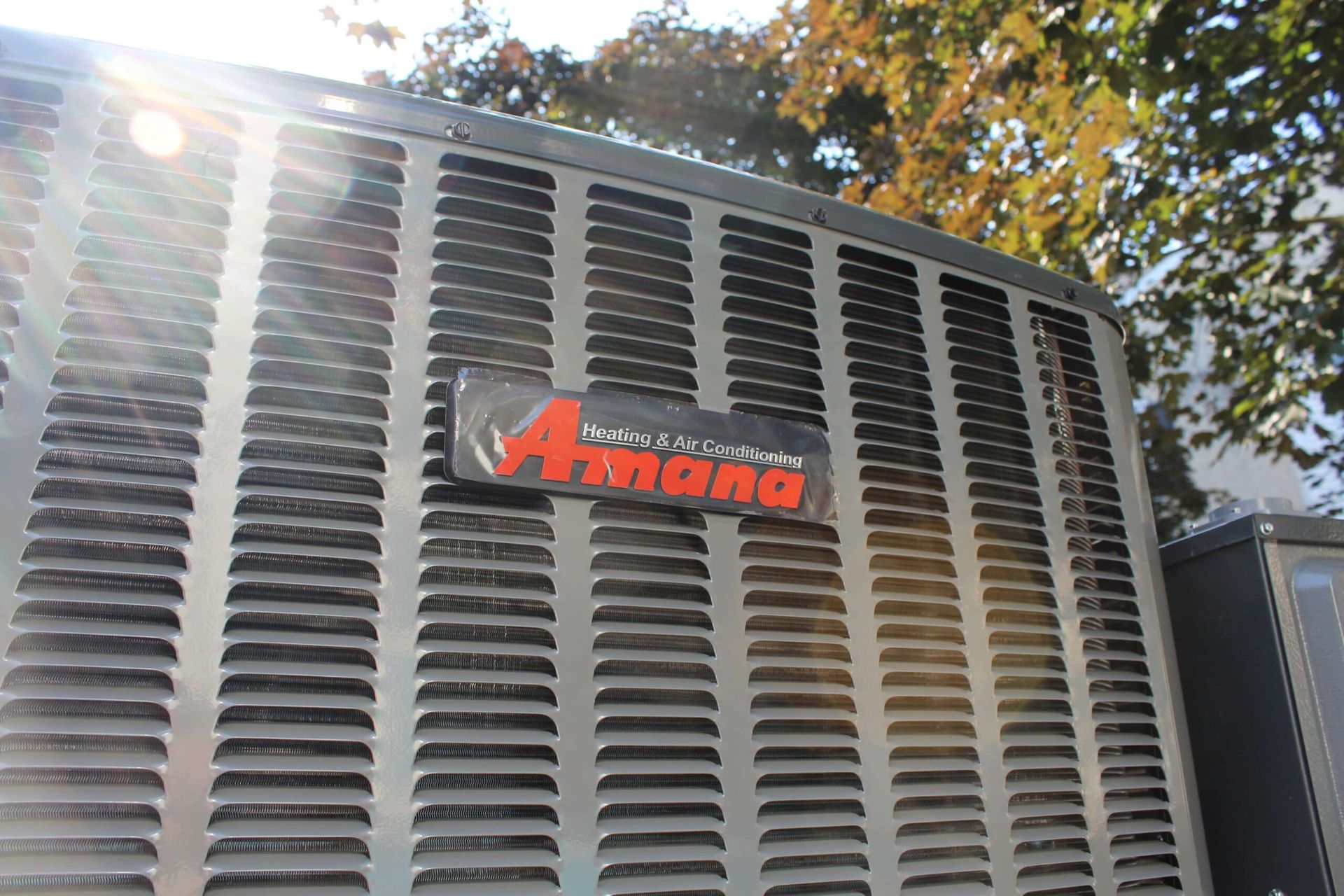 Contact Us Close-up of an Amana air conditioner unit in bright sunlight outdoors.