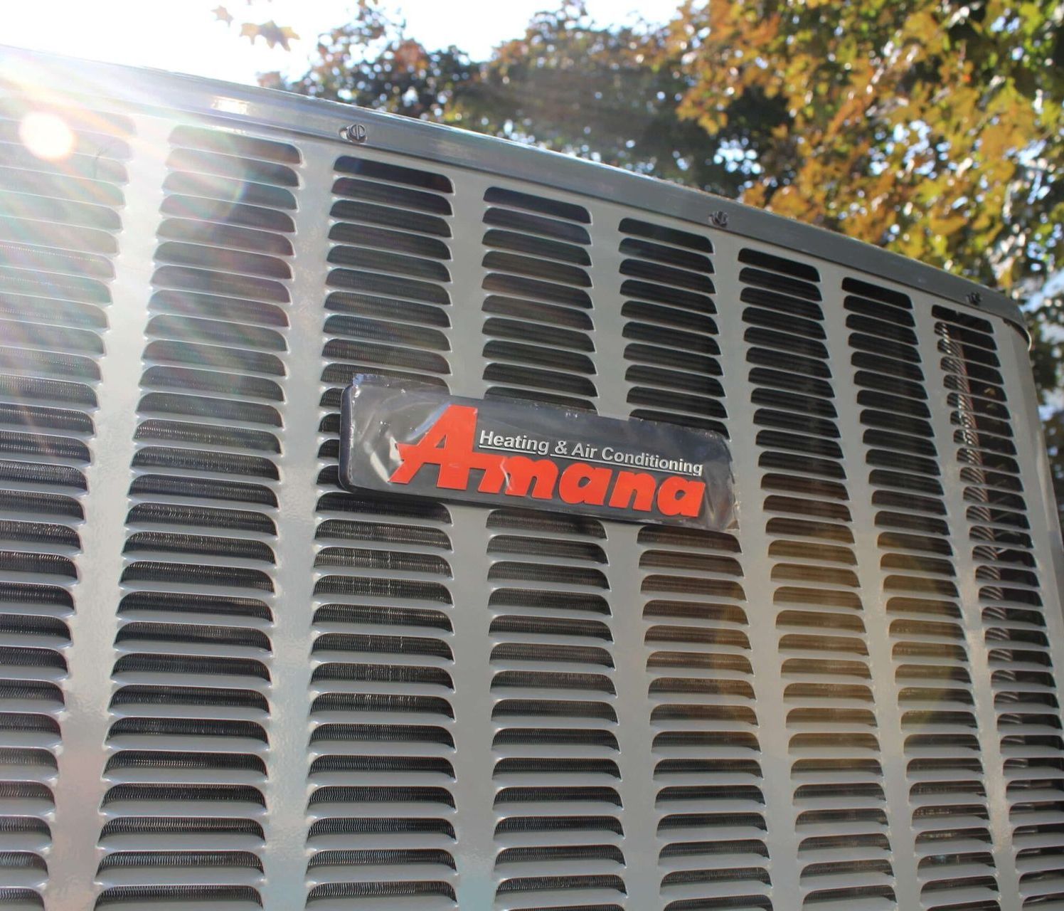 Close-up of an Avanta air conditioner grille with sunlight glare and autumn trees in the background