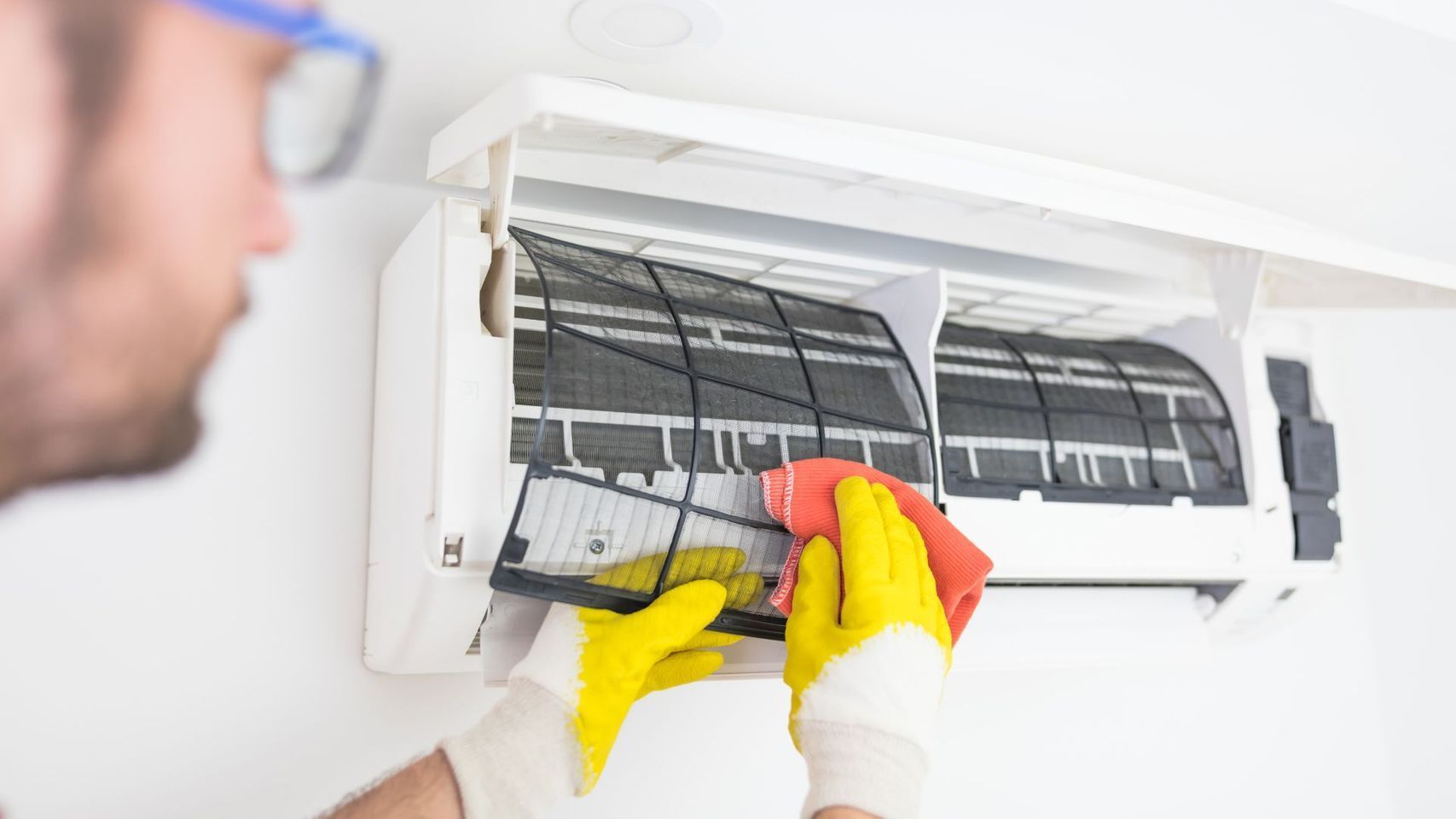 Technician cleaning a wall-mounted air conditioner with yellow gloves and red cloth
