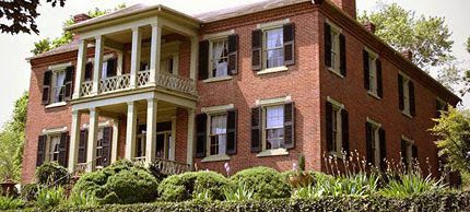 Brick historic house with white columns, black shutters, and a landscaped front yard