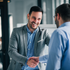 Two businessmen shake hands in an office, smiling during a friendly meeting.