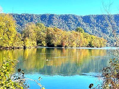 Autumn trees reflected in a calm blue lake beneath a forested hillside