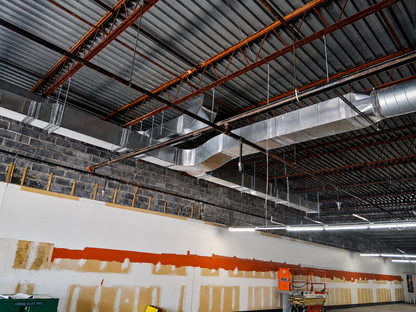 Warehouse interior with exposed ceiling beams, ductwork, and partially painted white walls under construction