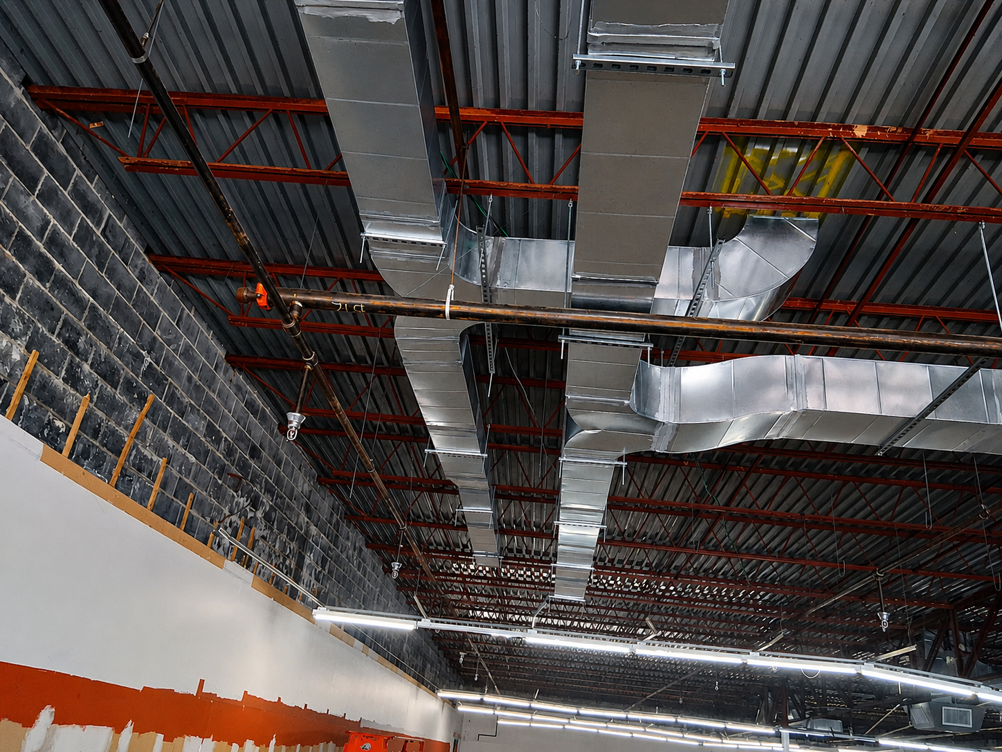 Industrial ceiling with exposed red conduit, silver ductwork, and insulation in a construction site
