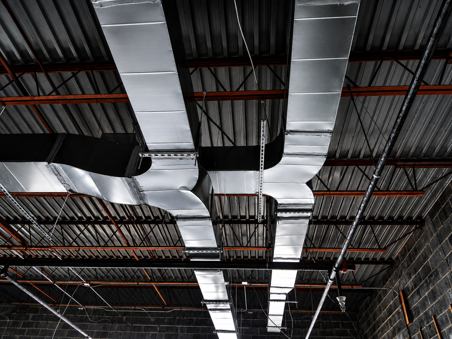Industrial ceiling with silver ductwork, black beams, and exposed metal framework in a warehouse