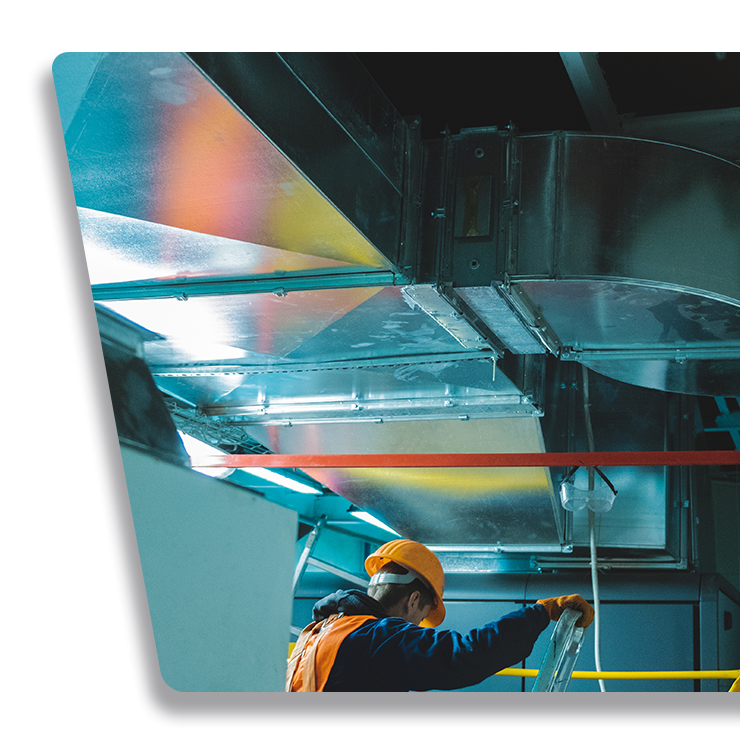 Contact Us Worker in orange hard hat inspecting metal ducting inside a modern industrial ceiling