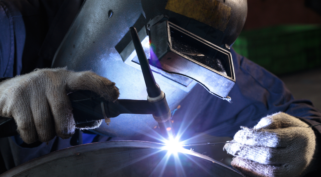 Our Services Welder in protective gear sparks bright blue light while joining metal pieces