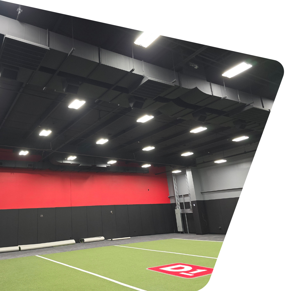 Contact Us Indoor turf training field with black ceiling, red-and-gray walls, and bright overhead lights