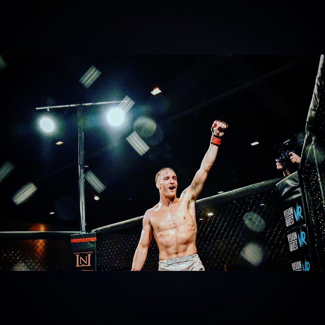 MMA fighter raises his arm in victory inside a lit octagon after a bout