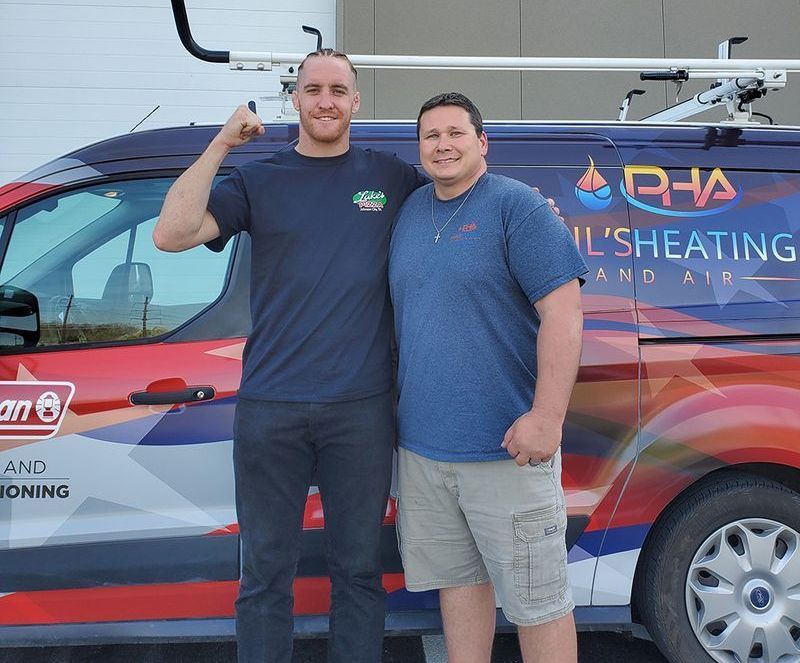 Two men standing beside a colorful HVAC service van, one flexing his arm and smiling.