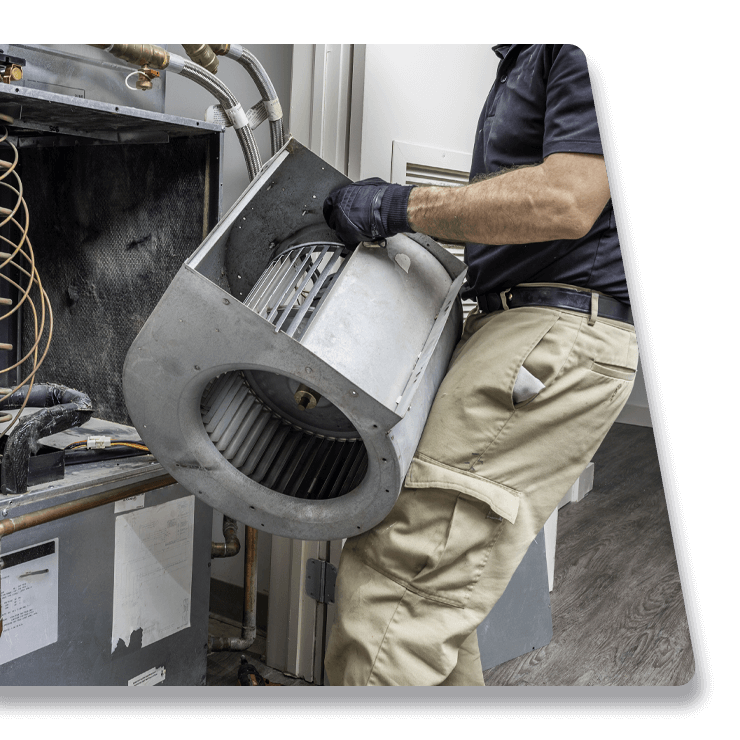 Technician lifting a large gray HVAC blower assembly in a maintenance room
