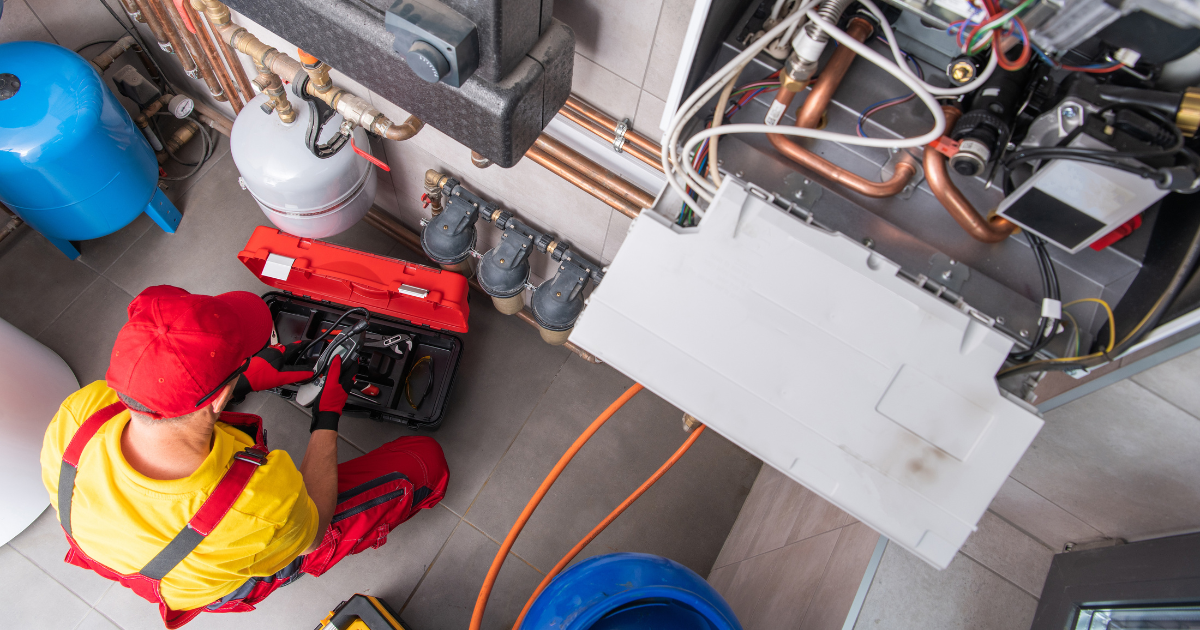 CONTACT US TO GET STARTED! Plumber in red and yellow working on heating system with tools.