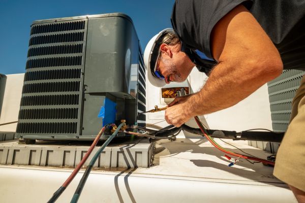 Worker repairing rooftop HVAC unit with tools and cables on a sunny roof