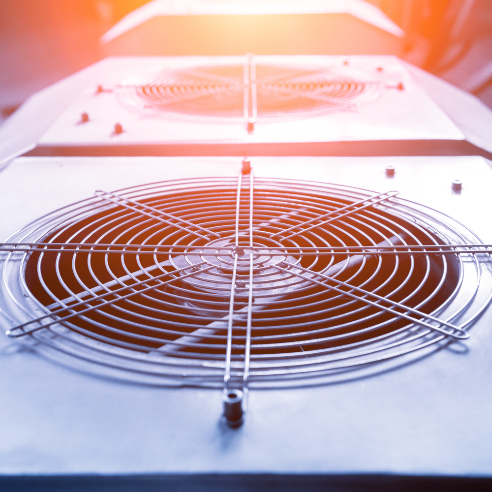 Close-up of a white industrial ventilation fan with circular metal grille, lit by warm orange light.