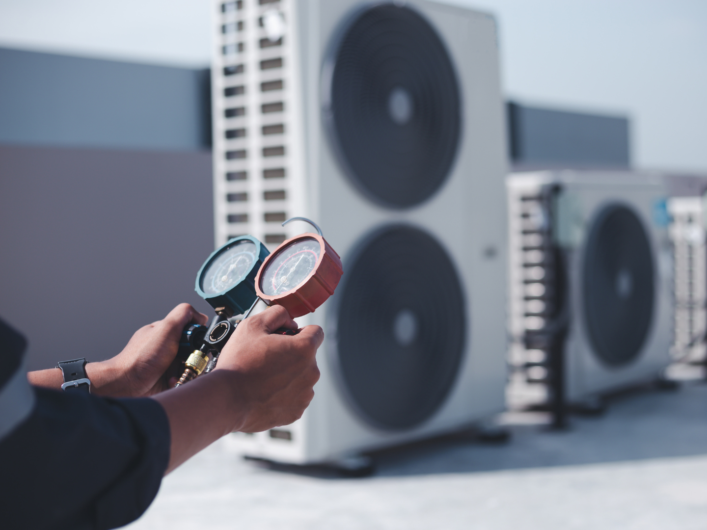Technician holding gauges near outdoor HVAC condenser units with fans