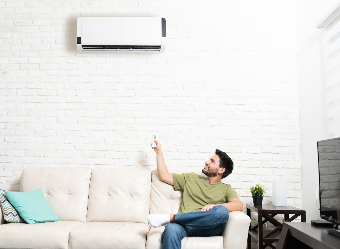 Man sitting on a sofa pointing at a wall-mounted air conditioner in a bright living room